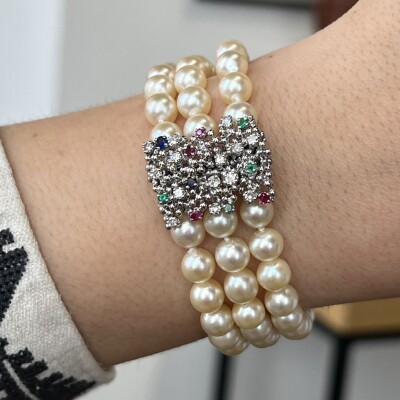 Bracelet 3 rangs en perles de culture. Fermoir en or blanc, saphirs, rubis, émeraudes et diamants