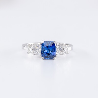 Bague en or blanc centre saphir bleu ovale accompagnée de deux diamants taillés en princesse